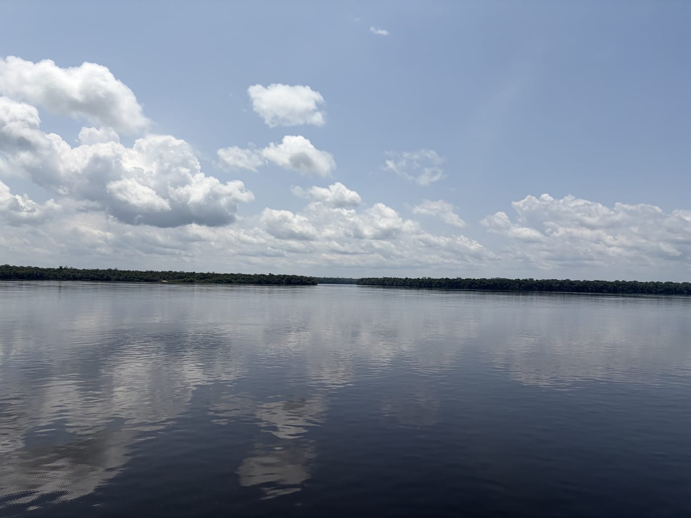 Céu e nuvens refletidos nas águas escuras de um rio da Amazônia