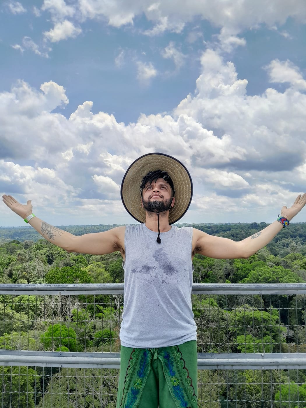 Keâ Costa de braços abertos em um mirante, com a floresta ao fundo
