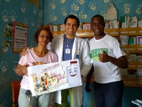 Profissionais de saúde com um cartaz, em sala decorada com mãos pintadas